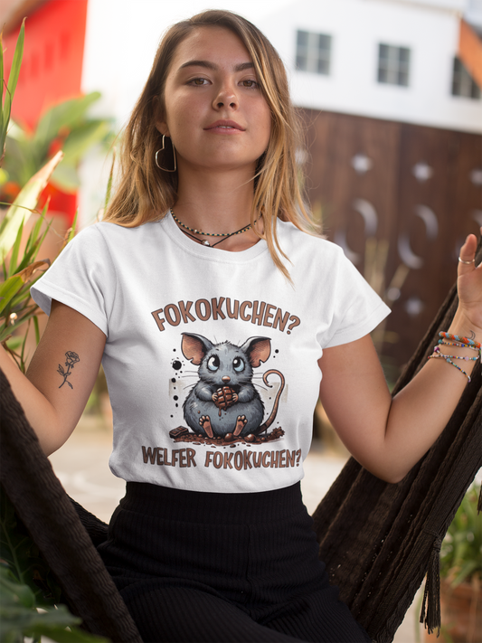 Blondes Mödchen trägt ein weißes Shirt mit Maus-Motib und Aufschrift "Fokokuchen? Welfer Fokokuchen?". Im Hintergrund ein verschwommenes Haus.