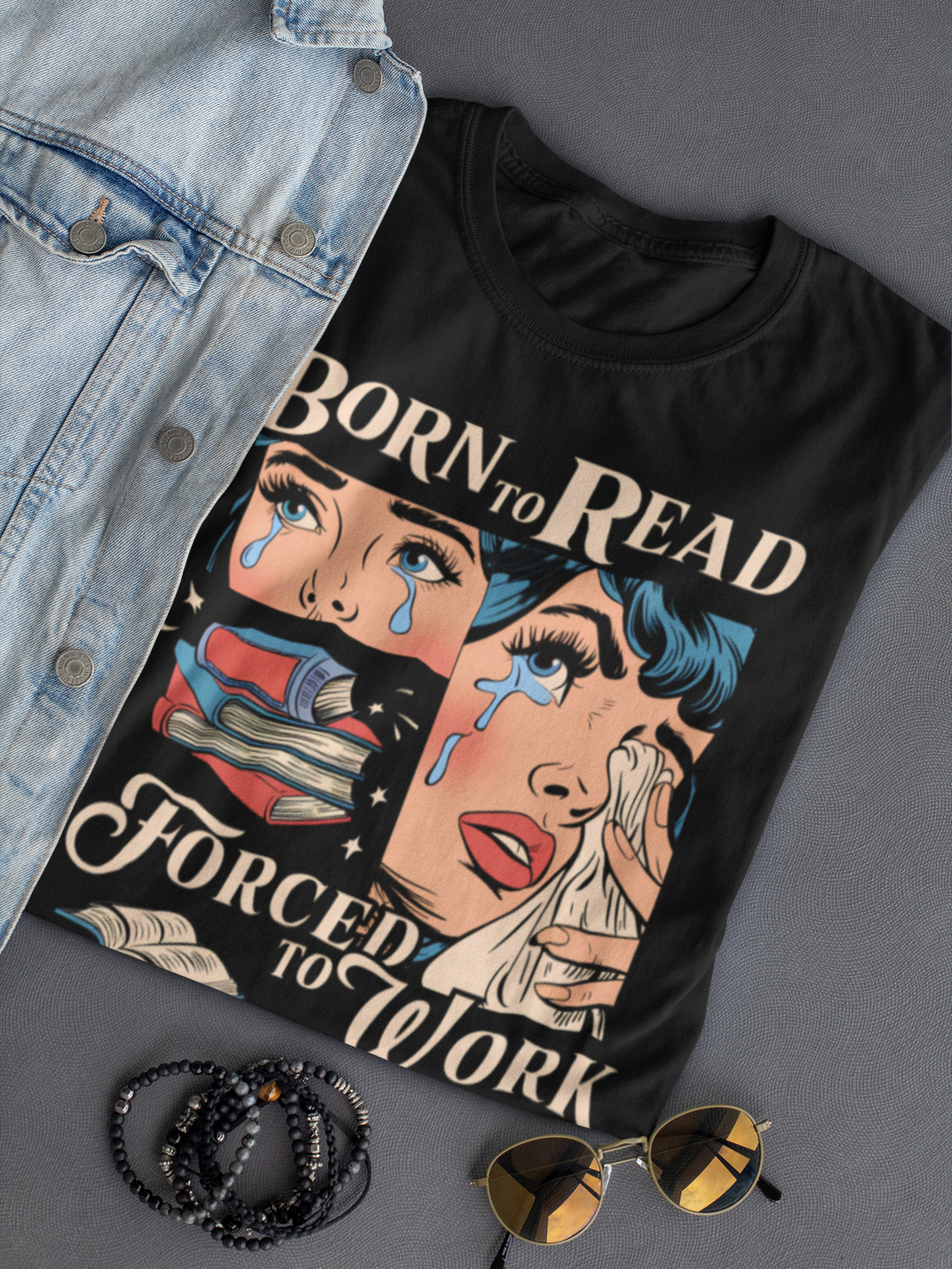 Schwarzes Ladies T-Shirt mit dem weißen Spruch „Born to read, forced to work“, zusammengelegt.