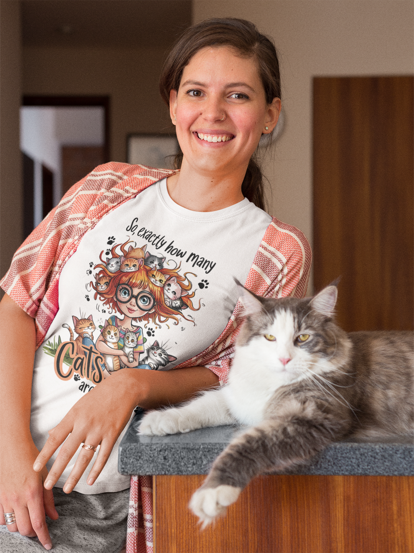 Frau mit Katze. Sie hat lange schwarze Haare und trägt ein Shirt mit Comic-Katze-Motiv. Ansicht Oberkörper.