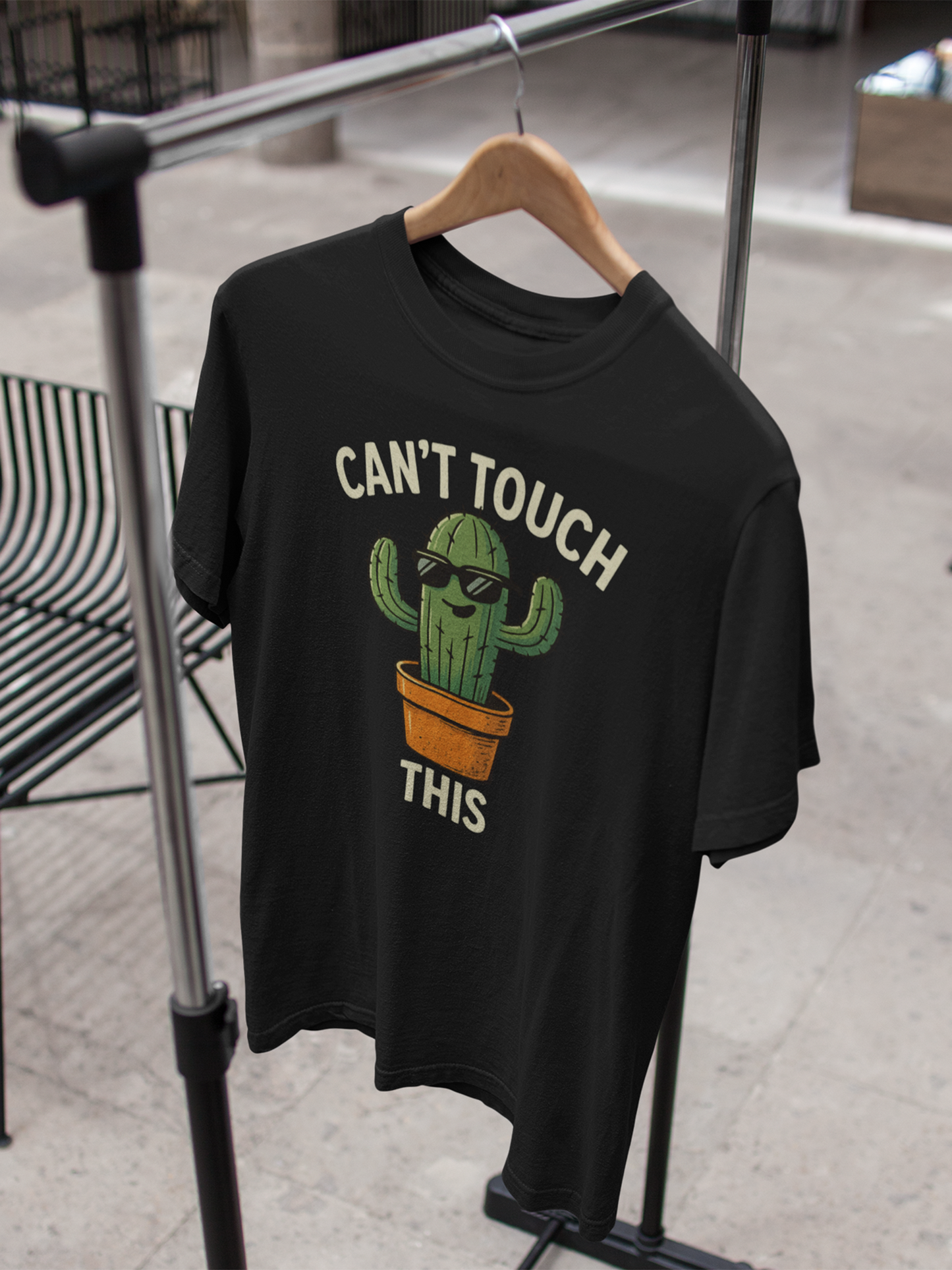 Schwarzes T-Shirt am Kleiderständer mit Cartoon-Kaktus und Spruch „Can’t Touch This“.