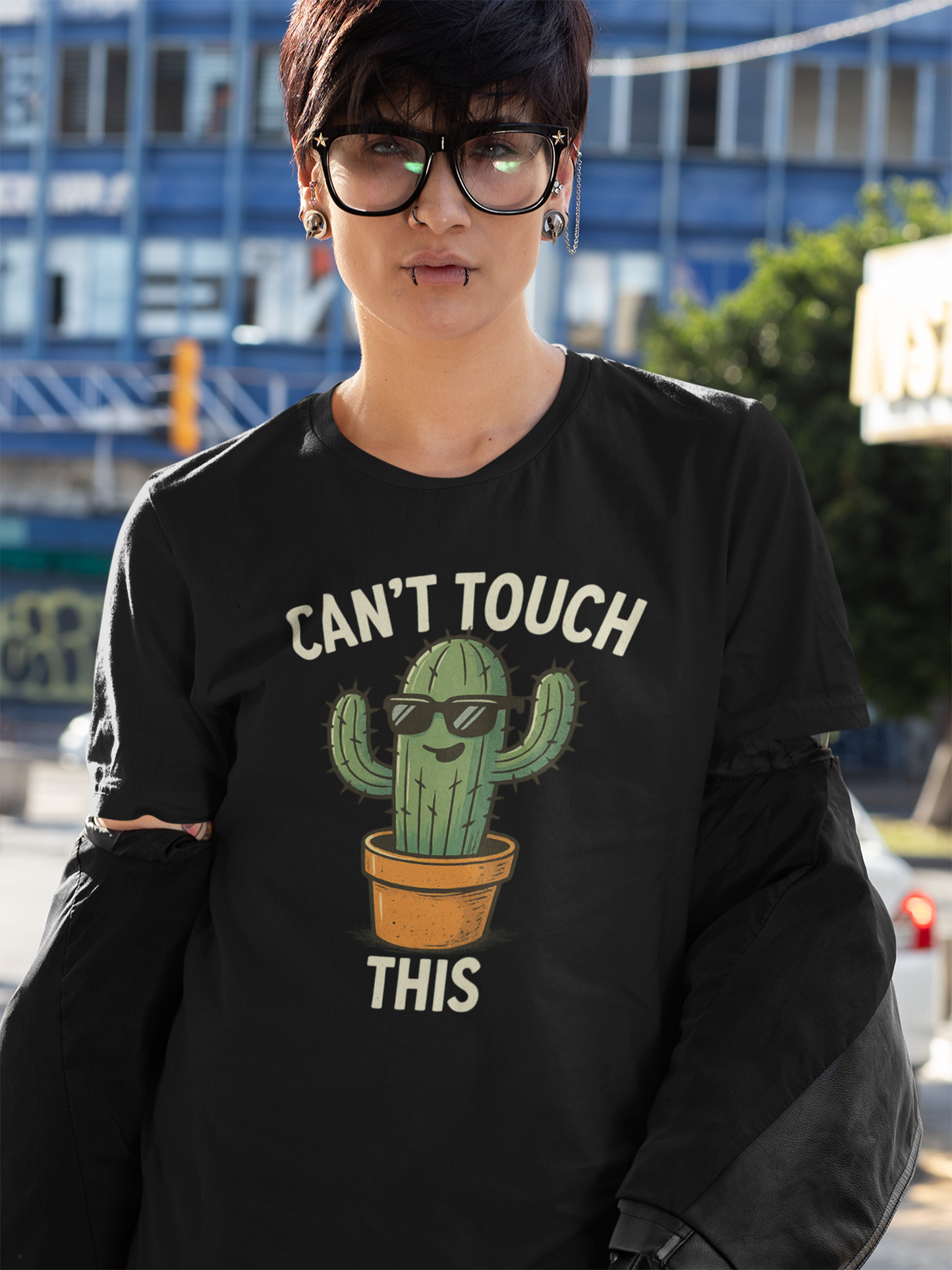 Frau mit großer schwarzer Brill. Sie trägt ein schwarzes T-Shirt mit Cartoon-Kaktus und Spruch „Can’t Touch This“.