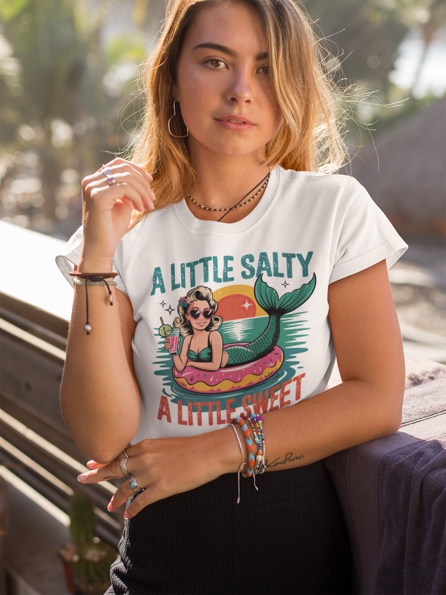 Blonde junge Frau mit weißem Shirt mit Aufschrift "A little salty" und Meerjungfra-Motiv.