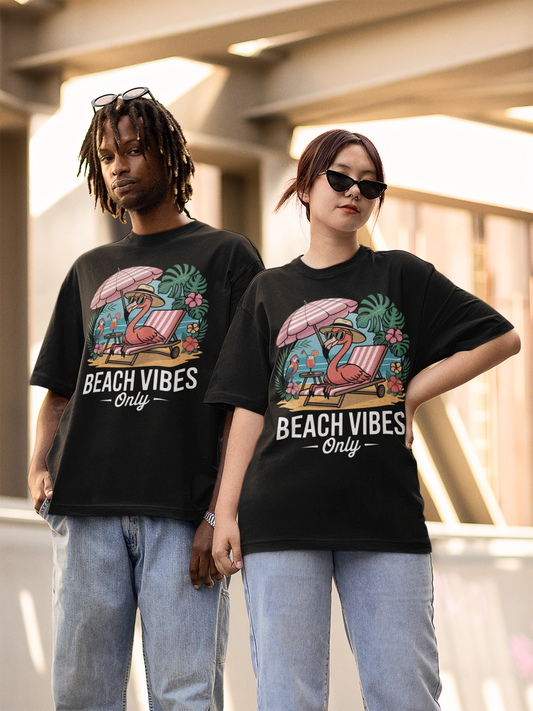 Junger Mann und junge Frau, stehen Beide tragen Jeanshose und beide tragen das selbe schwarze Shirt mit Aufdruck "Beach Vibes only" mit Flamingo unter Sonnenschirm.