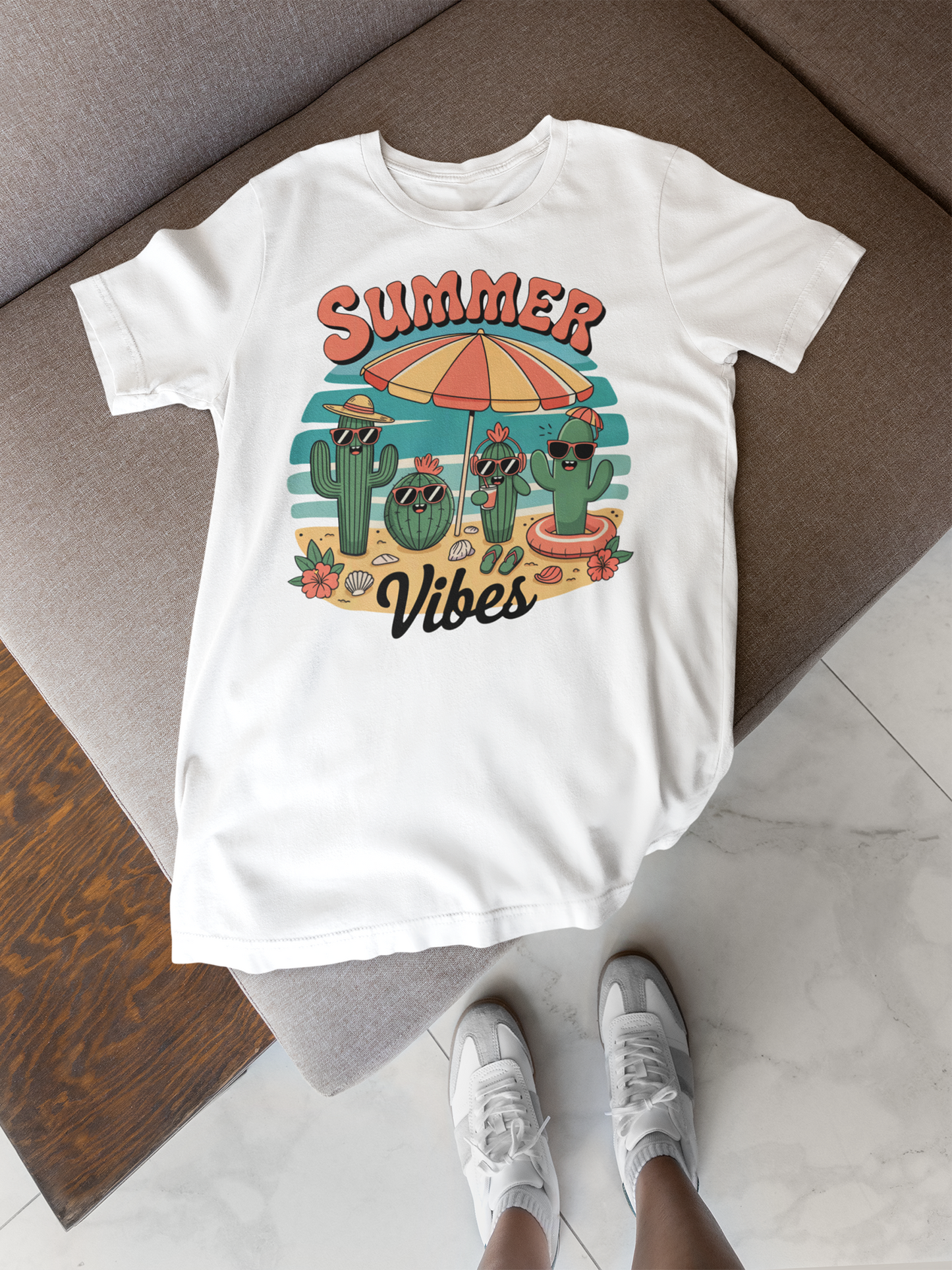 Weißes Shirt mit Kaktus-Print und Aufschrift "Summer Vibes" liegt auf Sofa. Unten im Bild sind Beine mit Turnschuhen zu sehen.
