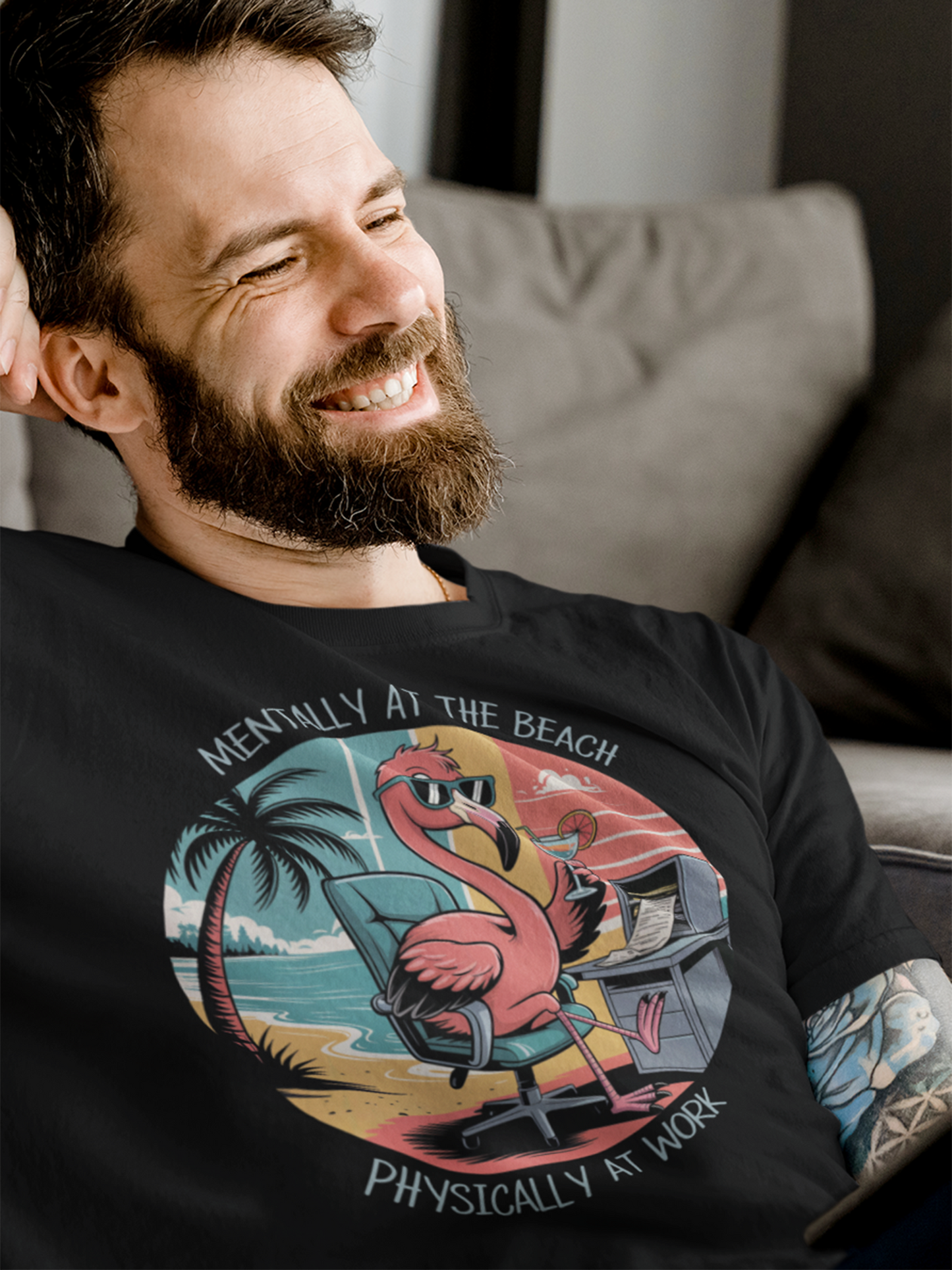 Lachender Mann mit Bart, trägt ein schwarzes Shirt mit Flamingo Büro Motiv.