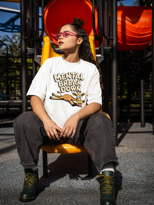 Junge Frau, sitzend auf Rutschbahn, trägt weißes T-Shirt mit Giraffe und dem Text „Mental Break Down“ (Ganzkörperaufnahme)