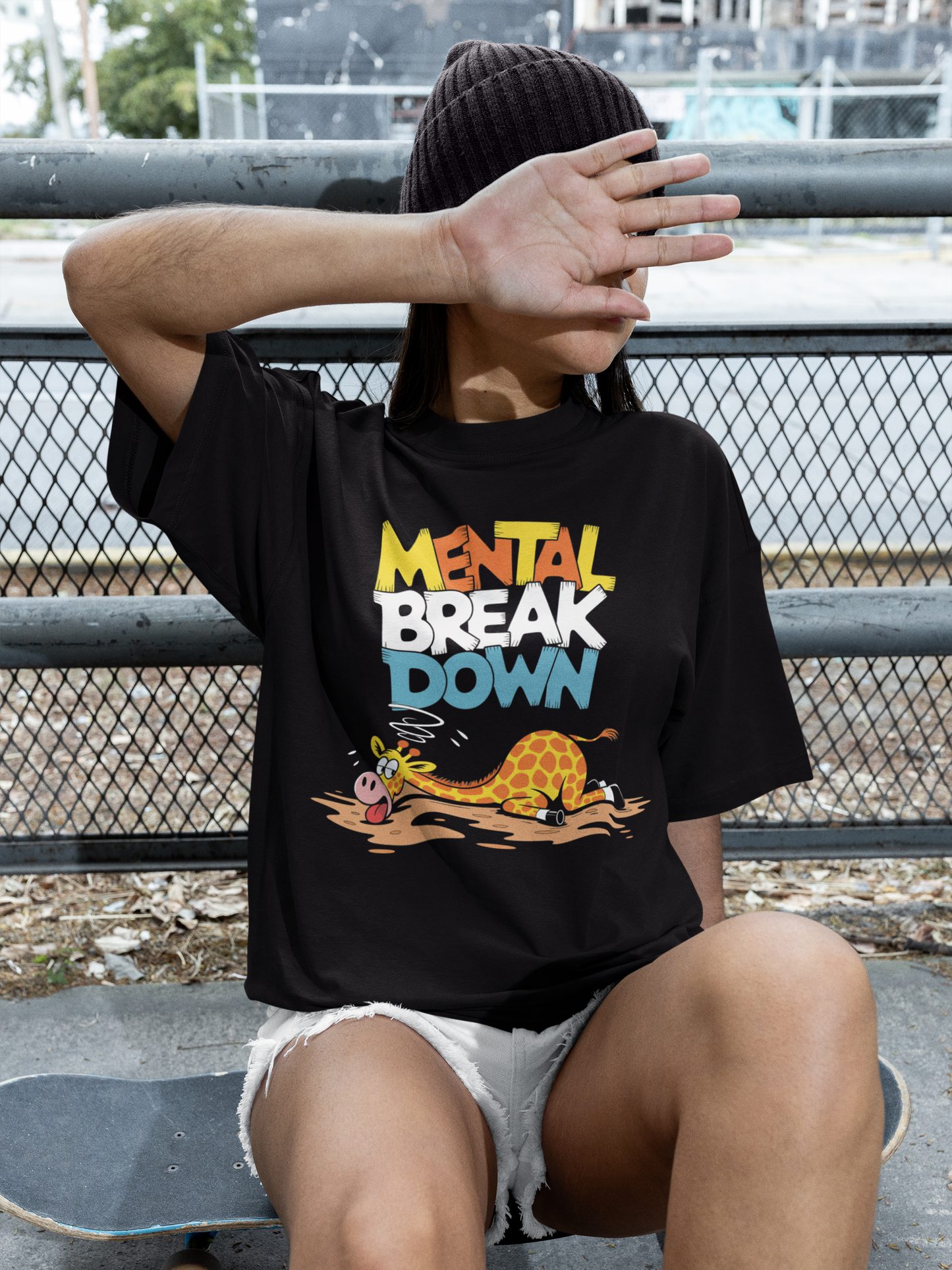 Junge Frau, sitzend, hält Arm vor das Gesicht. Sie trägt schwarzes T-Shirt mit Giraffe und dem Spruch „Mental Break Down“ (Oberkörperaufnahme)