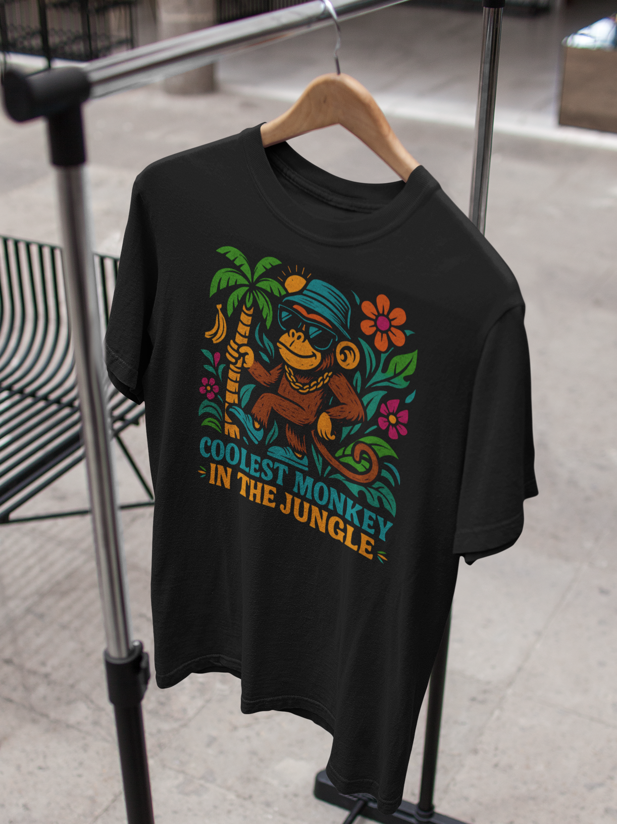 Schwarzes T-Shirt mit Retro-Affe und Schriftzug „Coolest Monkey in the Jungle“, hängend auf Kleiderständer.