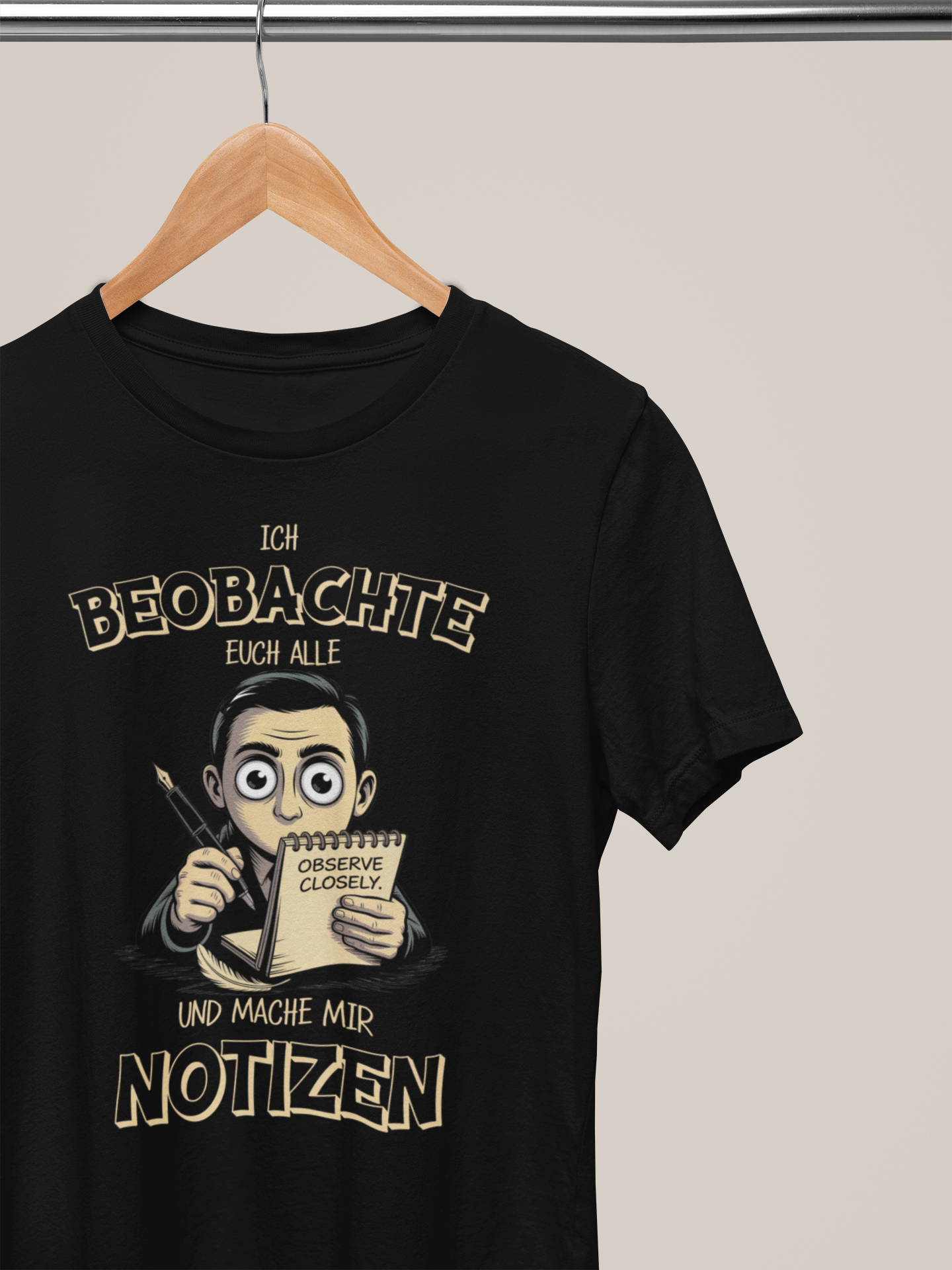 Schwarzes Shirt auf Kleiderbügel mit dem Spruch „Ich beobachte euch alle und mache mir Notizen“ (Oberkörperaufnahme)