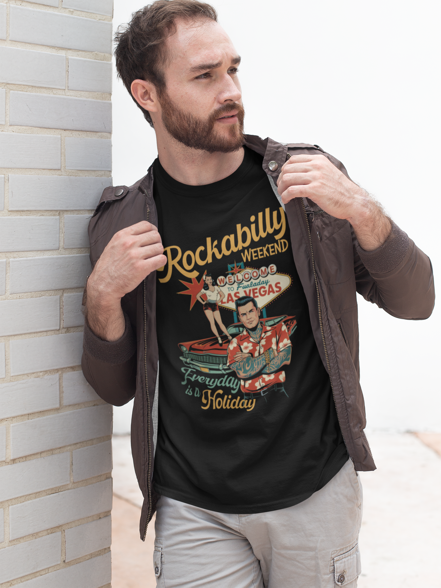 Junger Mann, an Wand gelehnt, mit offener Lederjacke, trägt schwarzes Shirt mit Rockabilly Weekend-Motiv im Retro-Style (Oberkörperaufnahme)