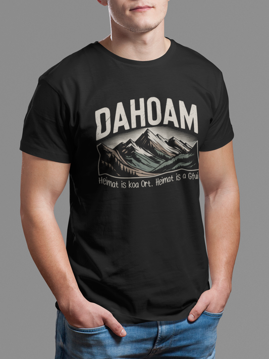 Mann trägt schwarzes T-Shirt mit Bergmotiv und Spruch „Dahoam – Heimat is koa Ort, Heimat is a Gfui“ (Oberkörper)