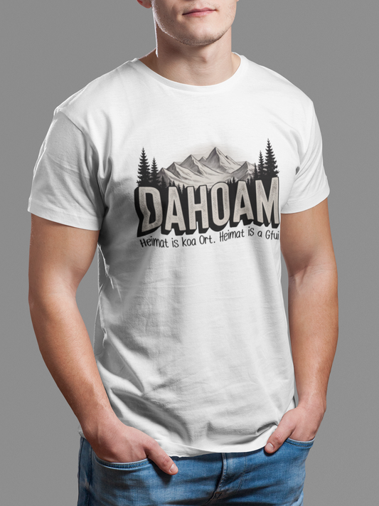 Mann trägt weißes T-Shirt mit Bergmotiv und Spruch „Dahoam. Heimat is koa Ort. Heimat is a Gfui“ (Oberkörper)