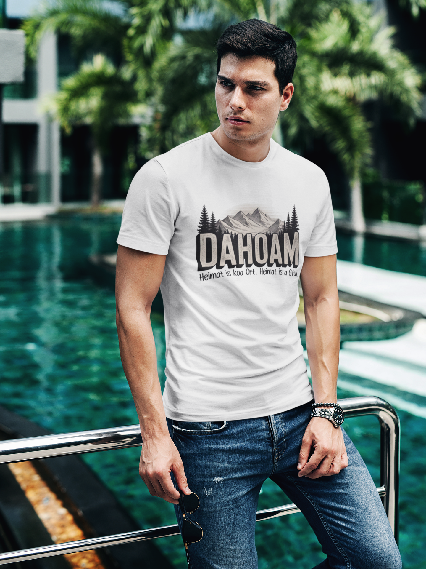 Mann trägt weißes T-Shirt mit Bergmotiv und Spruch „Dahoam. Heimat is koa Ort. Heimat is a Gfui“ (Oberkörper)