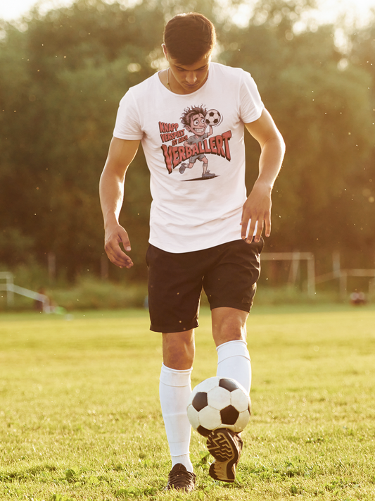 Mann spielt Fußball. Er trägt weißes T-Shirt mit Fußball-Motiv und Spruch „Knapp verspielt ist auch verballert“ (Ganzkörper)