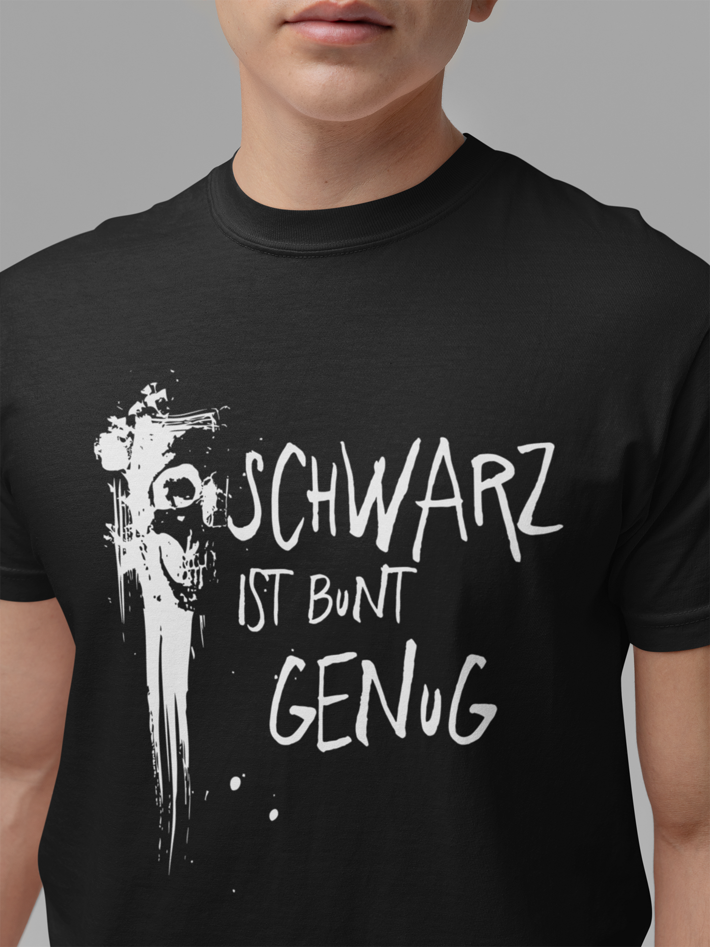Junger Mann trägt ein schwarzes T-Shirt mit Graffiti-Schädel und dem Text „Schwarz ist bunt genug“, Oberkörperansicht
