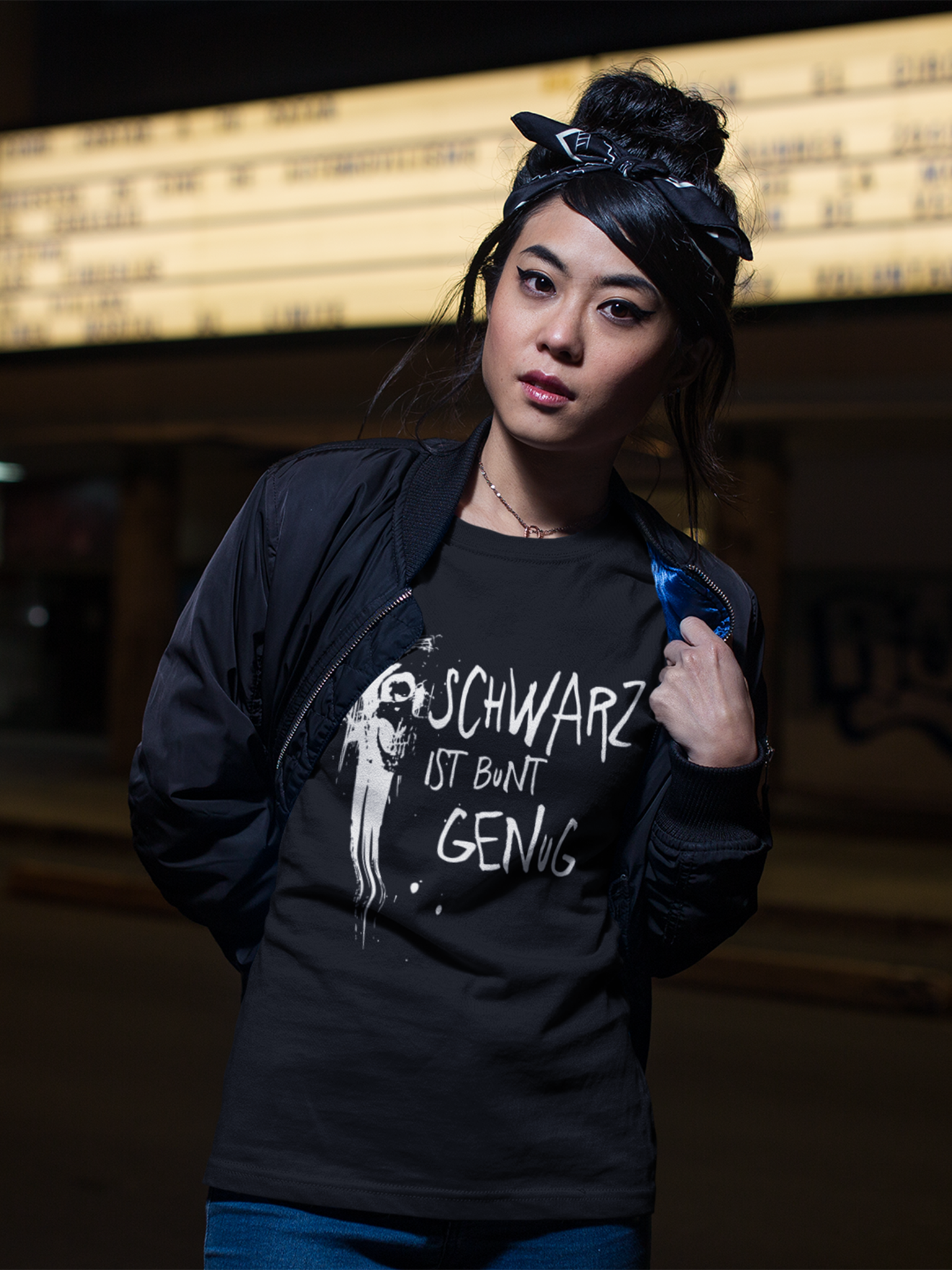 Junge asiatische Frau mit Hut trägt ein schwarzes T-Shirt mit Graffiti-Schädel und dem Text „Schwarz ist bunt genug“, Oberkörperansicht
