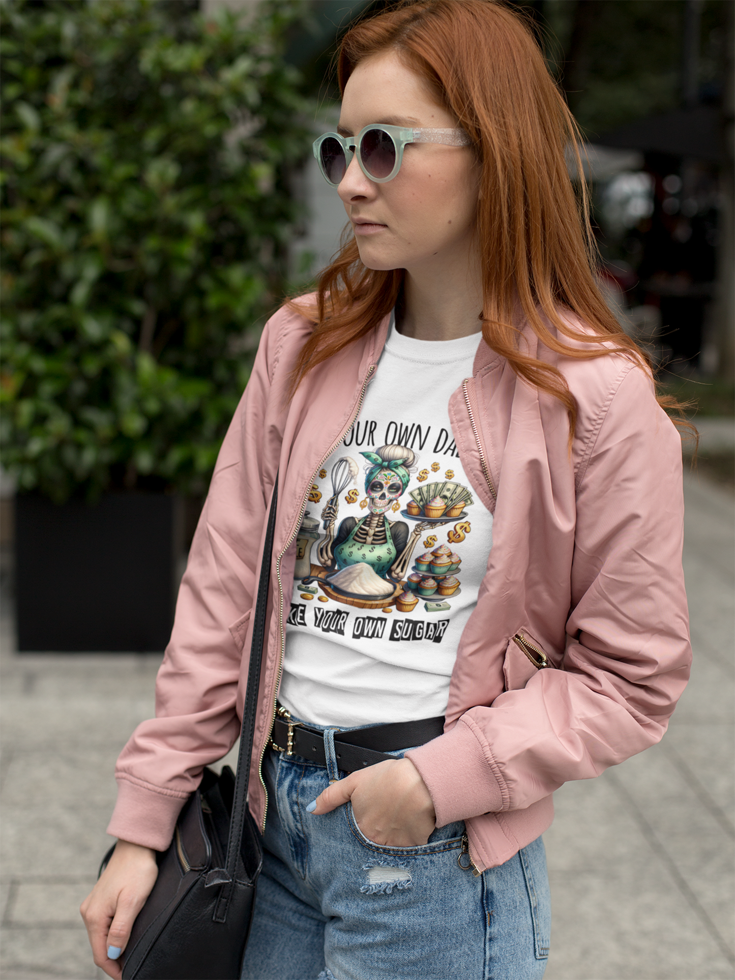 Frau mit Sonnenbrille und offener rosa Jacke trägt ein Shirt mit Skeleton-Girl-Motiv.