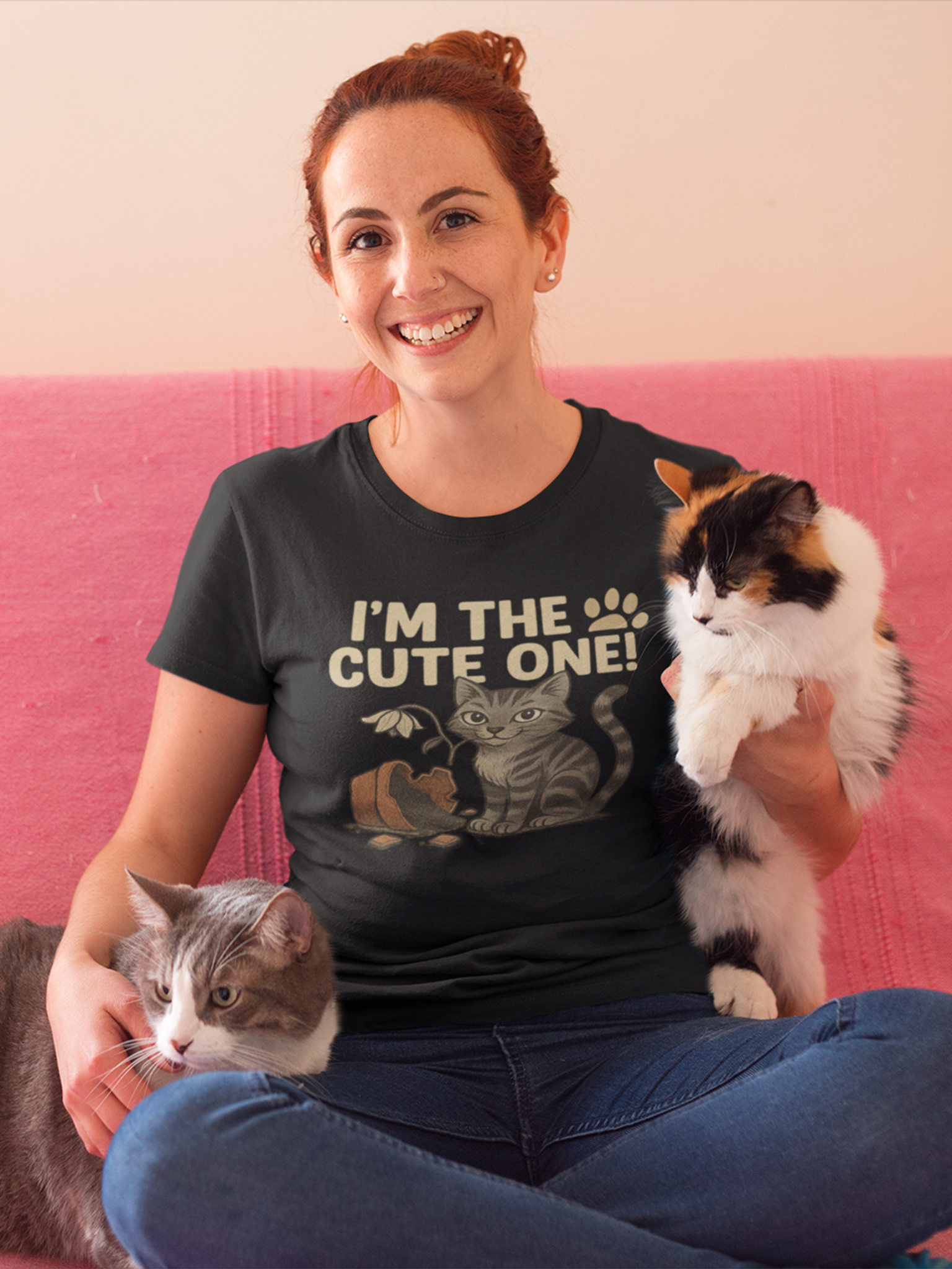 Frau sitzt auf Sofa und hat links und rechts eine Katze im Arm. Sie trägt ein schwarzes T-Shirt mit Katzenmotiv und der Aufschrift: "I´m the cute one!"