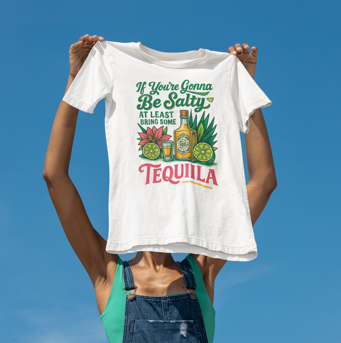 Jemand hält ein weißes T-Shirt mit tropischem „Bring Tequila“-Motiv vor sich in die Kamera