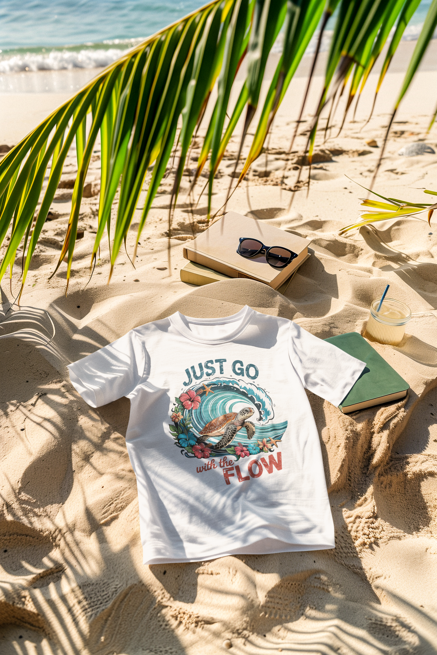 Palmenblatt am Stand. Im Sand Liegt ein weißes T-Shirt mit Retro-Print.