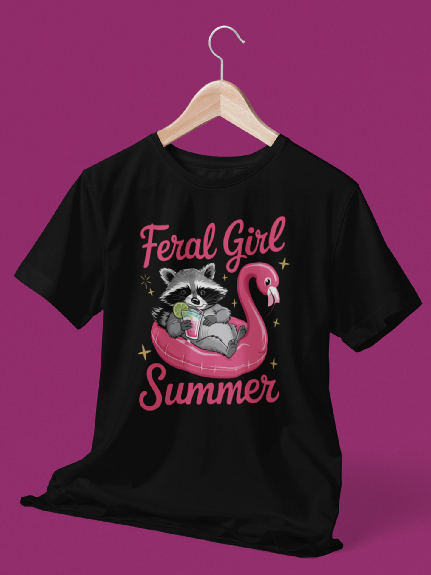 Schwarzes T-Shirt mit Waschbär auf pinkem Flamingo-Schwimmreifen, Cocktail in der Pfote und Schriftzug „Feral Girl Summer“