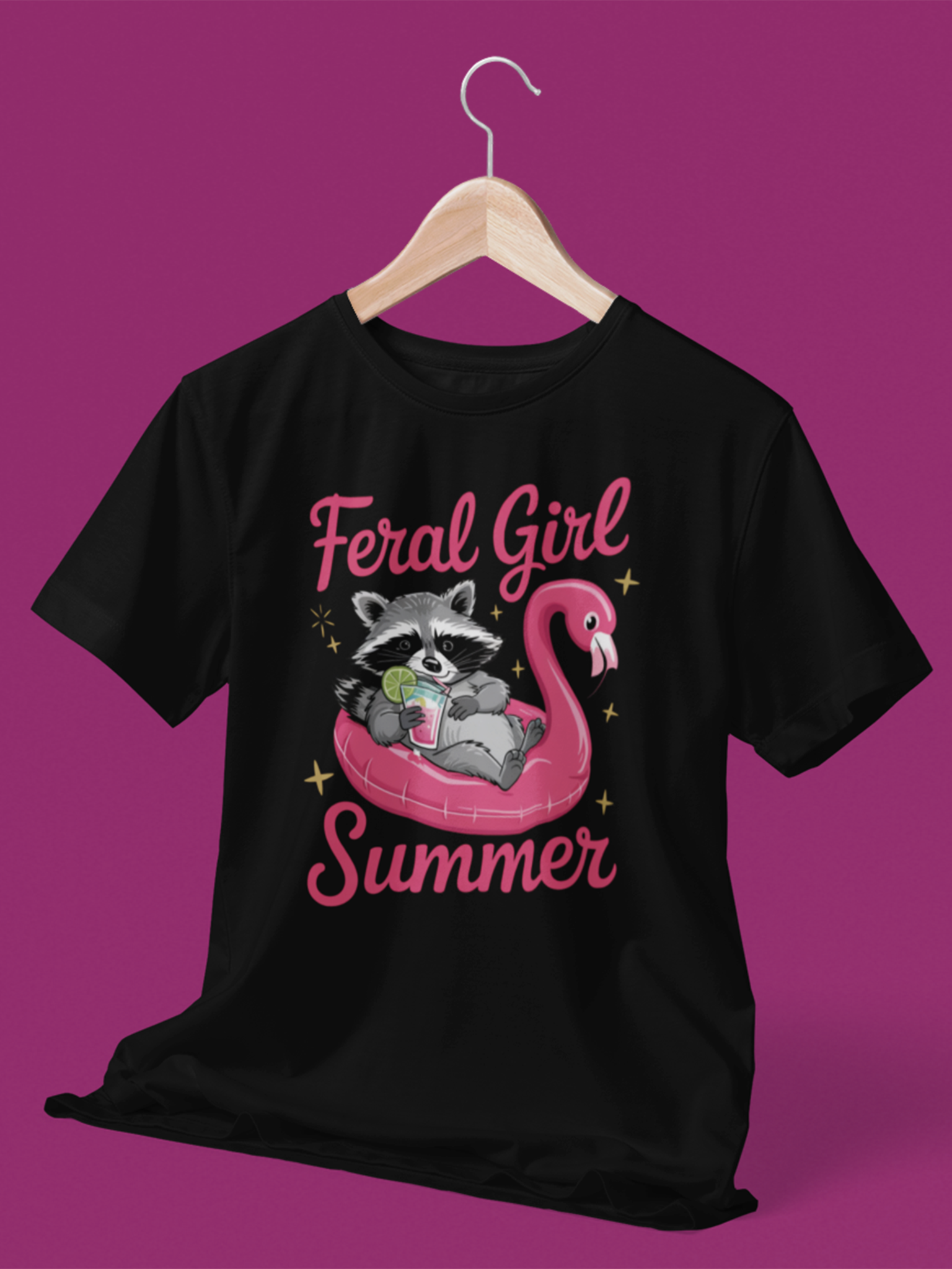 Schwarzes T-Shirt mit Waschbär auf pinkem Flamingo-Schwimmreifen, Cocktail in der Pfote und Schriftzug „Feral Girl Summer“