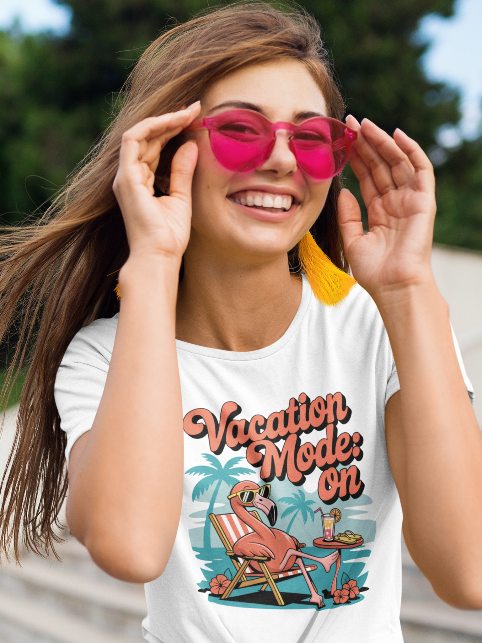Lachende junge Frau mit Sonnebrille trägt ein weißes T-Shirt mit dem Motiv „Vacation Mode: On“ und einem Flamingo mit Sonnenbrille, Oberkörperansicht