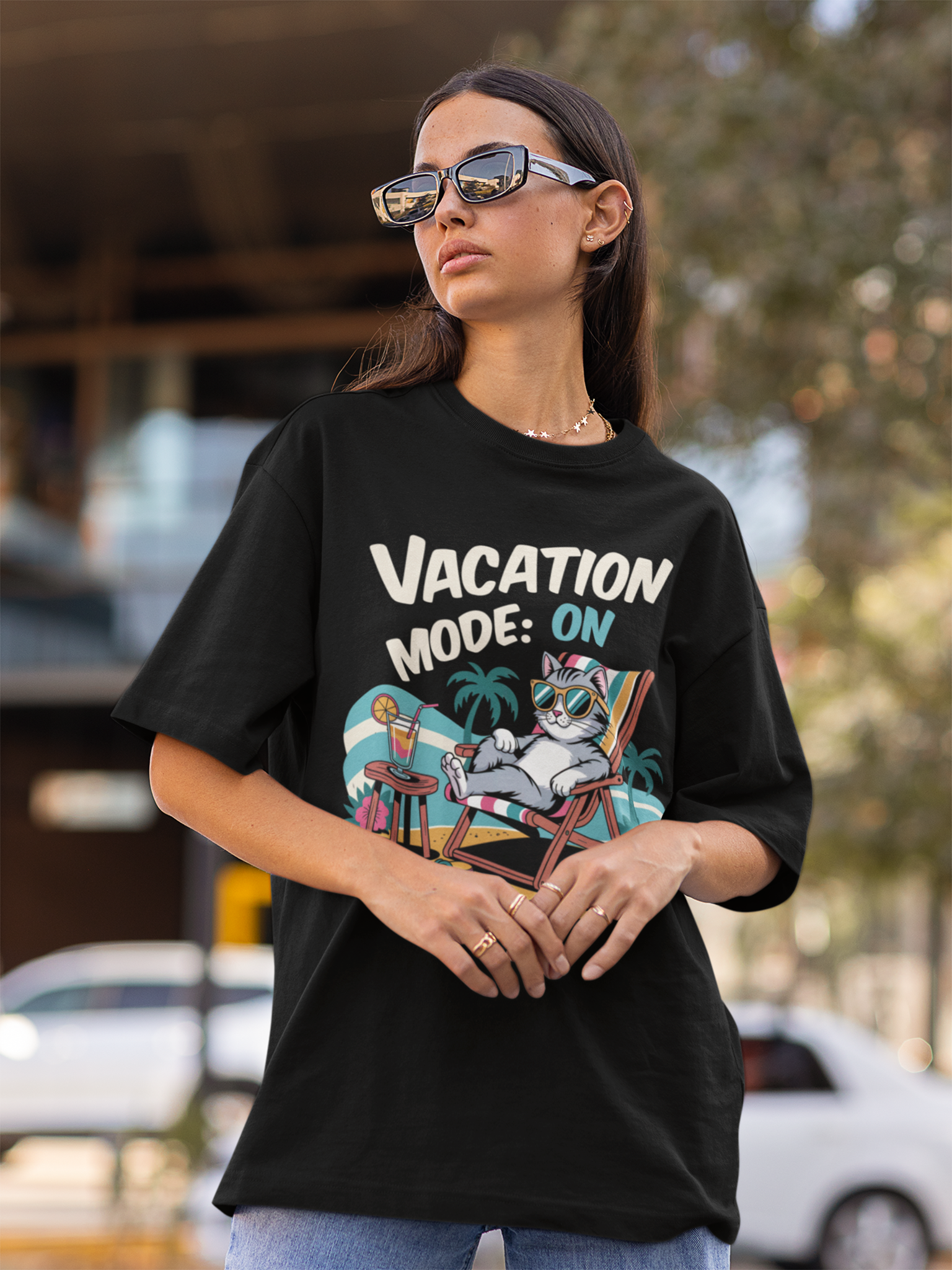 Junge Frau mit Sonnebrill trägt ein schwarzes T-Shirt mit Comic-Motiv einer relaxenden Katze mit Sonnenbrille und dem Text „Vacation Mode On“