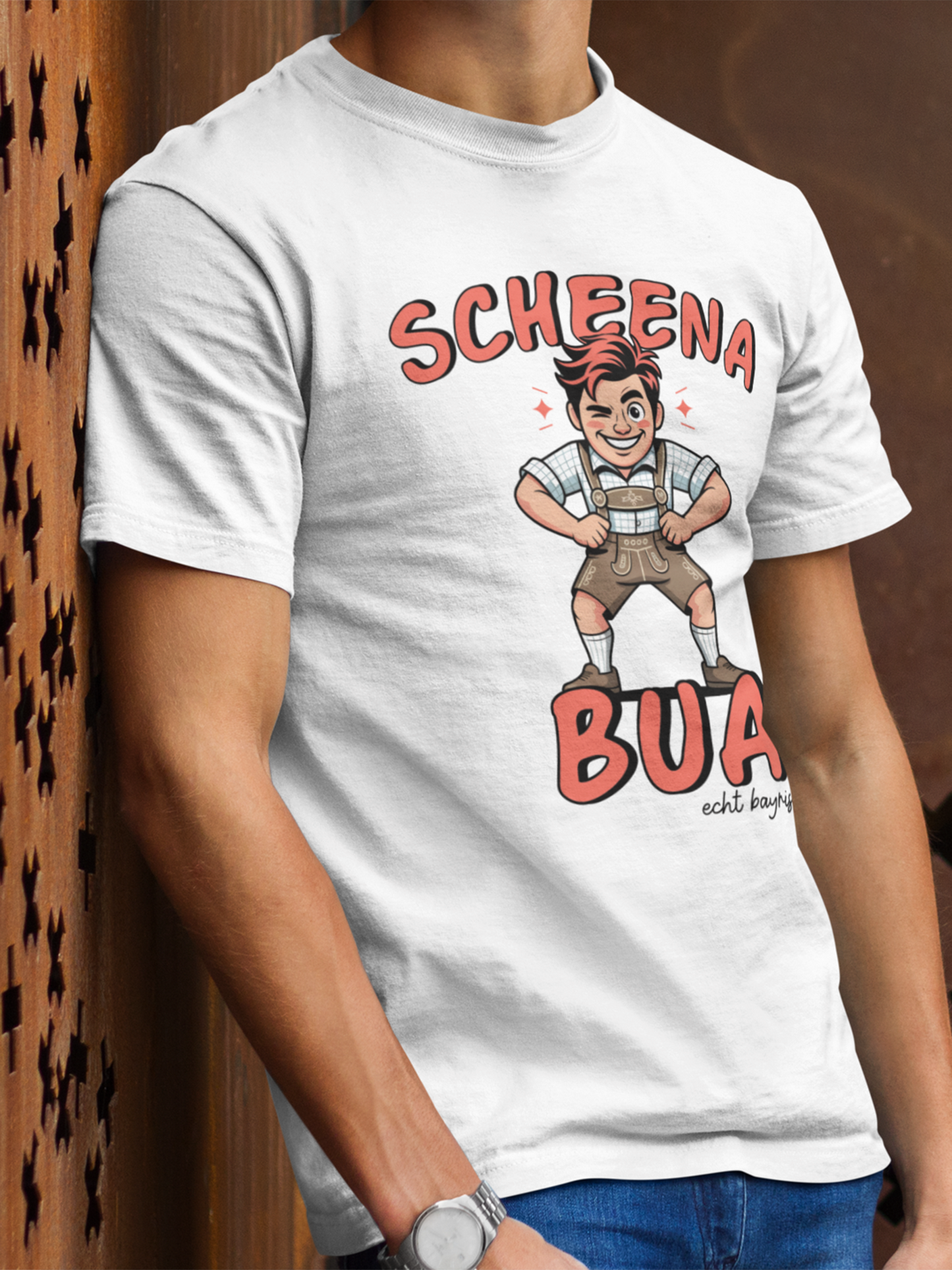 Oberkörperansicht einen jungen Mannes. Er trägt ein weißes T-Shirt mit weißem bayerischen Schriftzug „Scheena Bua“ und bayrischer Comic-Figur