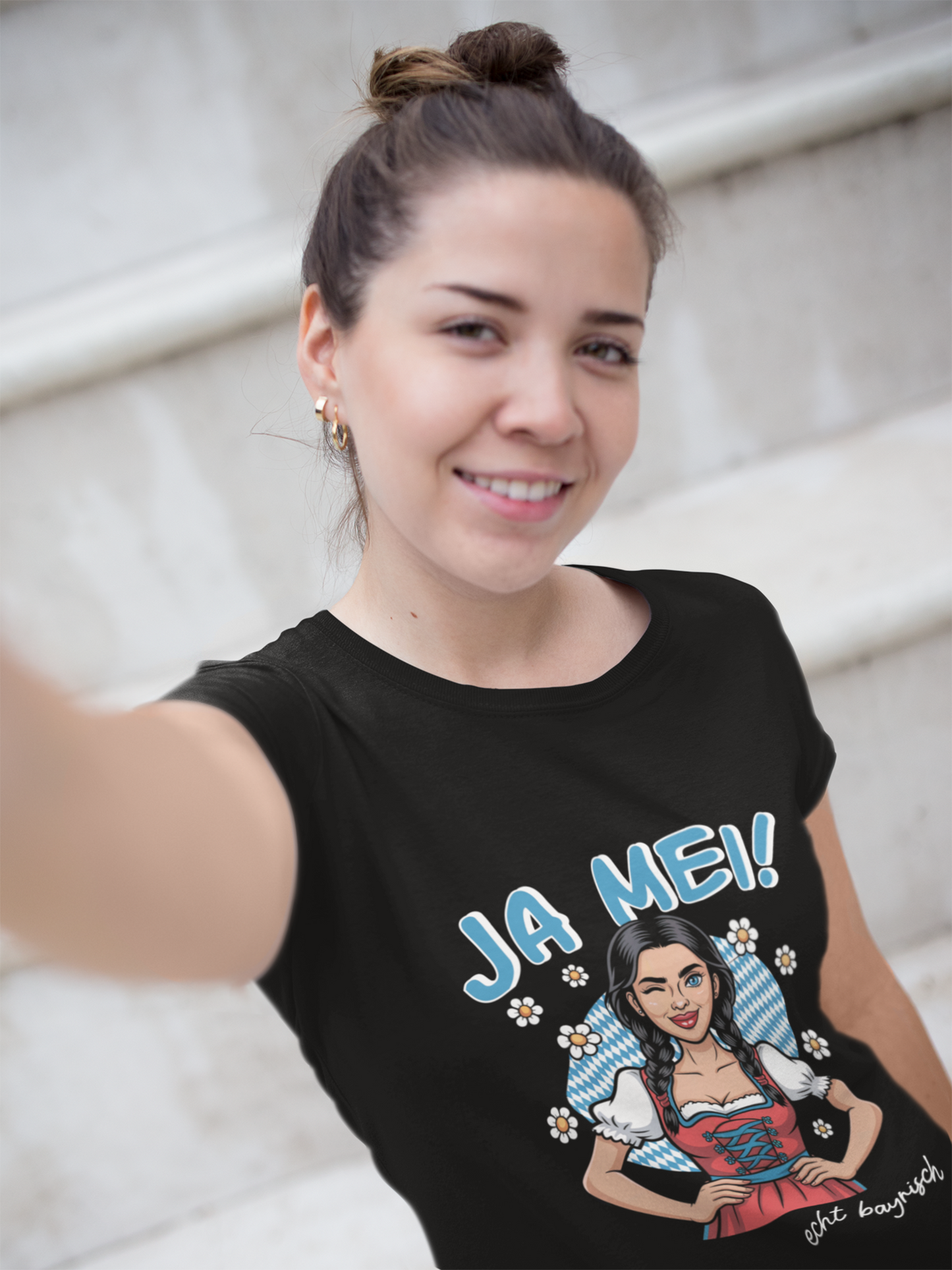 Junge Frau macht Selfie, sie trägt schwarzes T-Shirt mit dem bayerischen Spruch „Ja mei“, Oberkörperansicht