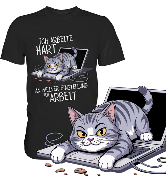 Schwarzes T-Shirt mit Comic-Motiv einer genervten Katze und dem Spruch „Ich arbeite hart an meiner Einstellung zur Arbeit“. Rechts vorne im Bild eine vergößerte Darstellung des Katzen-Motivs.