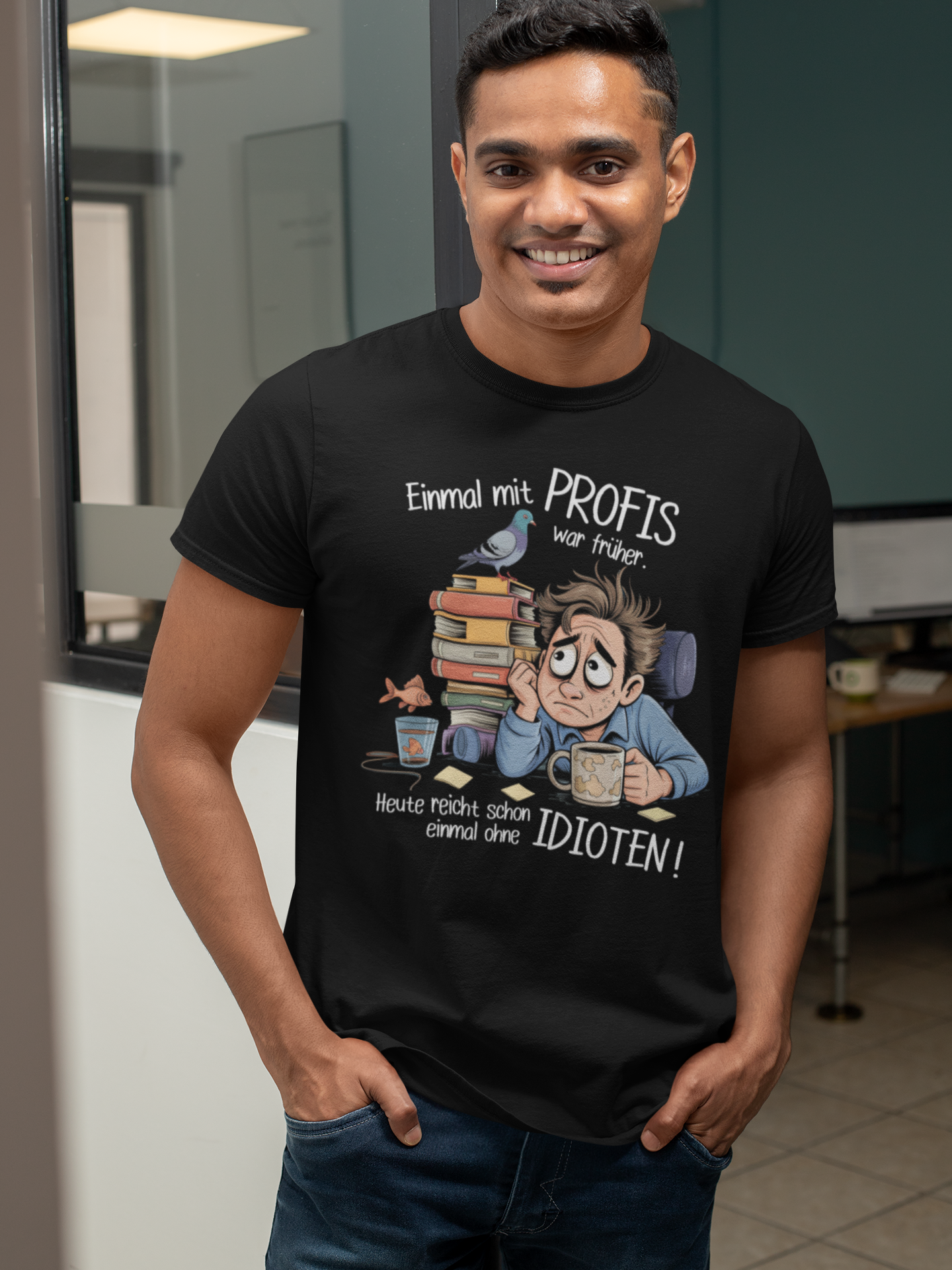 Junger Mann trägt schwarzes Shirt mit dem Spruch „Einmal mit Profis war früher – Heute reicht schon ohne Idioten“ und Büro-Motiv. (Oberkörperaufnahme)