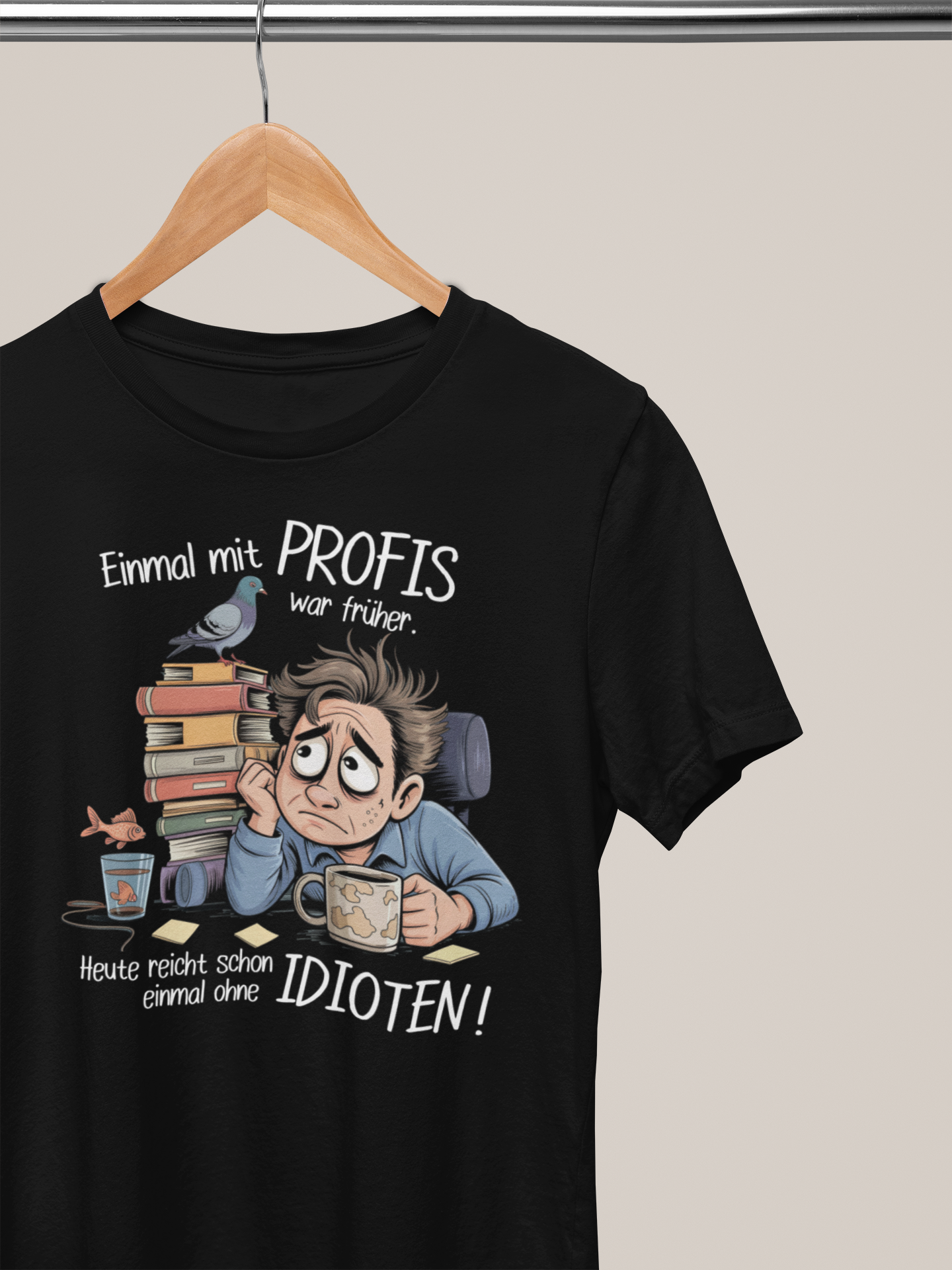 Schwarzes T-Shirt auf Kleiderbügel mit weißem Spruch „Einmal mit Profis war früher – Heute reicht schon ohne Idioten“ und Comic-Büro-Motiv.
