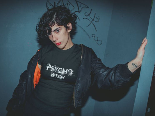 Androgyne Frau trägt schwarzes T-Shirt mit psychedelischem Schriftzug „Psycho Bitch“ – sie wirkt wild, provokant
