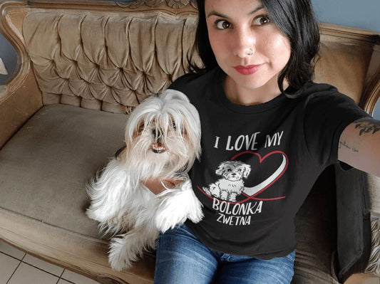 Junge Frau hält kleinen weißen Hund, Bolonka, im Arm und macht ein Selfie.