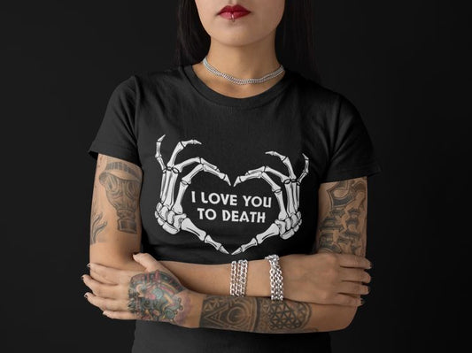 Tättowierte Gothic Frau trägt schwarzes T-Shirt mit Skeletthänden, die ein Herz formen, und dem Spruch „I love you to death“ – düster-romantisch im Gothic-Stil.